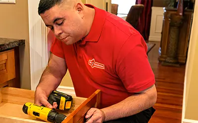 Male Mr. Handyman technician fixing a drawer with a drill.